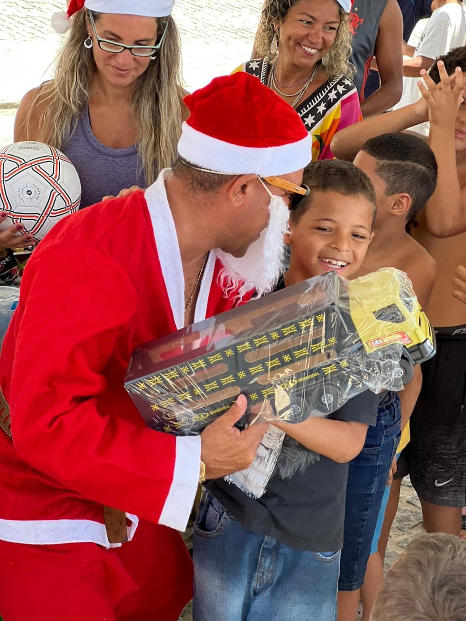 Entrega de presentes de Natal para crianças da comunidade, em ação da Recreio Solidário na praia do Recreio.